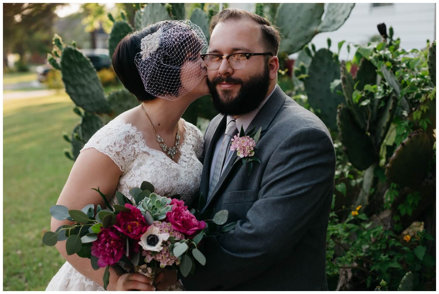 Bride kissing grooms cheek in front of a cactus.